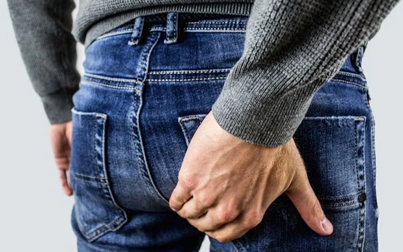 Man in blue jeans holding his buttock in pain with his right hand