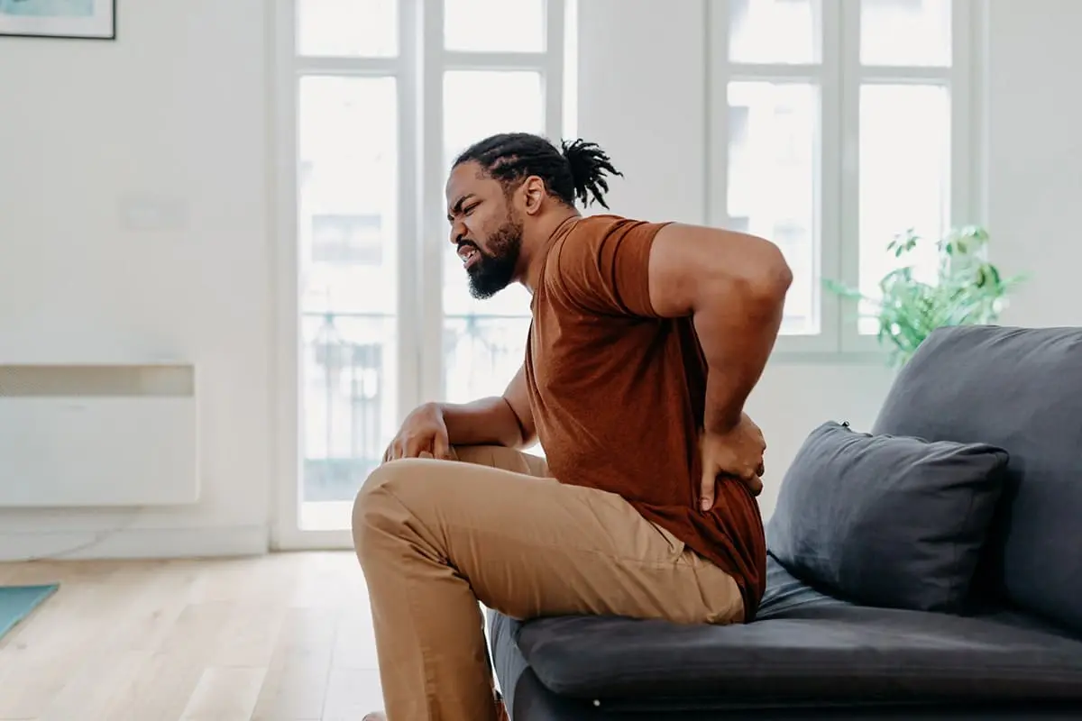 Young black man seating on a cushioned chair holding his lower back in pain from his sacroiliac joint