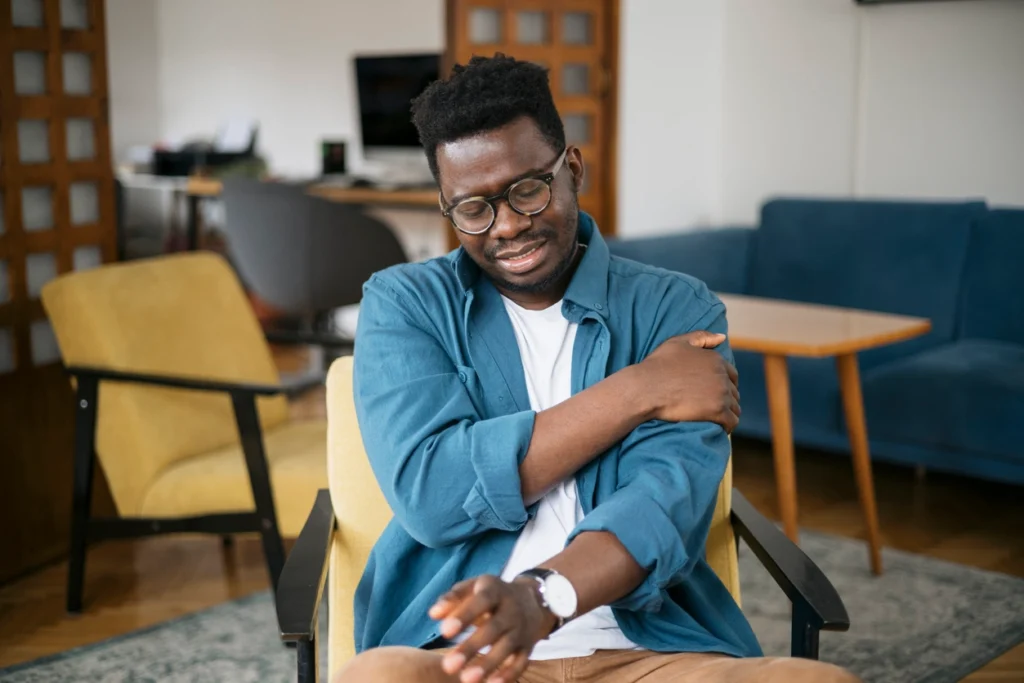 Young black man sitting in a living room, holding his left arm in pain.