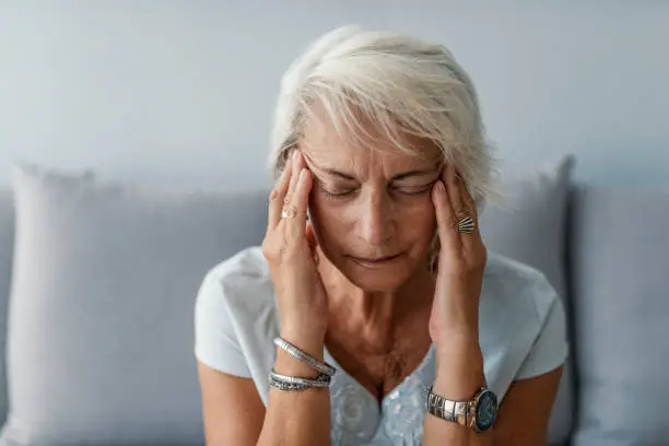 Woman experiencing back of head and neck pain while holding head with both hands